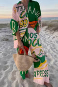 Model on a beach in a pink-and-green graphic-print linen shirt and wide-leg pants set