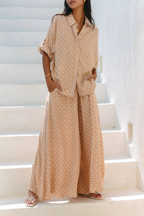 Woman in a tan geometric tile-print linen shirt and wide-leg pants set on white steps