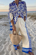 Model on a beach in a cream and blue sardine-print shirt and wide-leg pants two-piece set