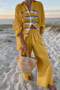 Model on a beach in a yellow linen short-sleeve shirt with mackerel fish print and wide-leg pants