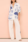 Model in a white short-sleeve camp shirt with blue Grecian embroidery and wide-leg pants set