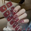 Hand with deep-red holiday nail wraps featuring white snowflakes, gold lines and small stars