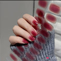 Hand wearing glossy jelly wine-red semi-cured gel nail strips beside the strip sheet