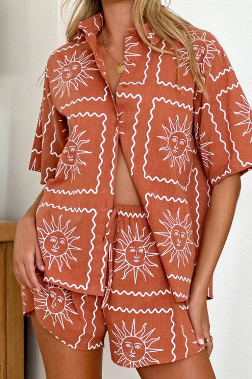 Model on a beach in a coral-and-green graphic-print long-sleeve shirt and matching shorts set