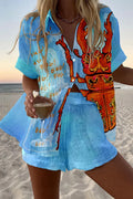 Model on a beach in a blue watercolor short-sleeve shirt and shorts set with an orange lobster print