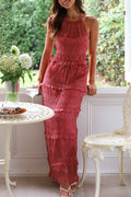 Model in a coral textured halter top and tiered ruffle maxi skirt two-piece set at a garden table